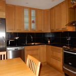 kitchen featuring range oven, range hood, dishwasher, stainless steel refrigerator, light hardwood floors, dark countertops, and brown cabinets